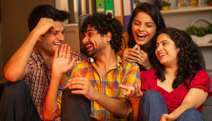 A group of four young friends laughing and enjoying a fun conversation indoors, creating a joyful and relaxed atmosphere.