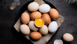Fresh brown and white eggs arranged on a dark surface with one cracked yolk, used to explain are eggs dairy and their role in nutrition and allergies.