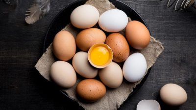 Fresh brown and white eggs arranged on a dark surface with one cracked yolk, used to explain are eggs dairy and their role in nutrition and allergies.