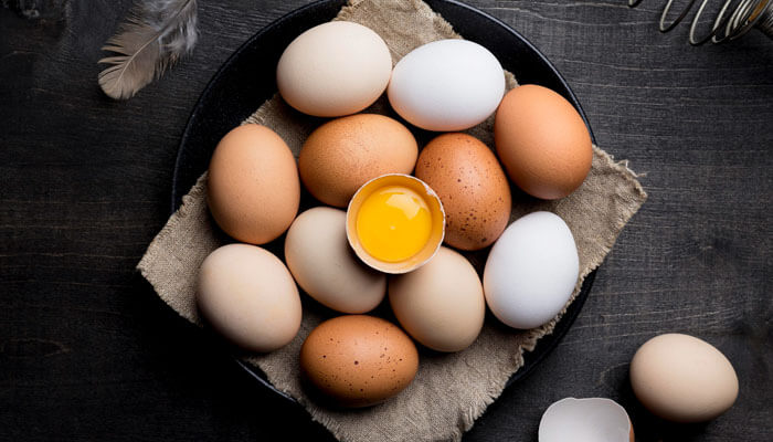 Fresh brown and white eggs arranged on a dark surface with one cracked yolk, used to explain are eggs dairy and their role in nutrition and allergies.