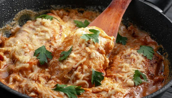 Oven-baked Marry Me Chicken in creamy sauce topped with parsley and sun-dried tomatoes in a white baking dish.