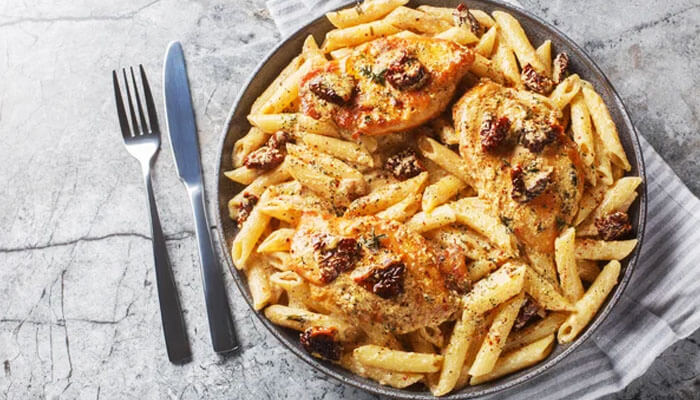 Bowl of creamy Marry Me Chicken pasta with penne, sun-dried tomatoes, and golden chicken breasts served with cutlery.
