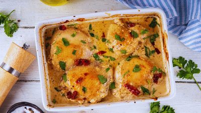 Oven-baked Marry Me Chicken in creamy sauce topped with parsley and sun-dried tomatoes in a white baking dish.