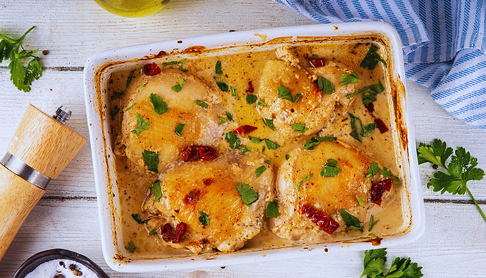 Oven-baked Marry Me Chicken in creamy sauce topped with parsley and sun-dried tomatoes in a white baking dish.