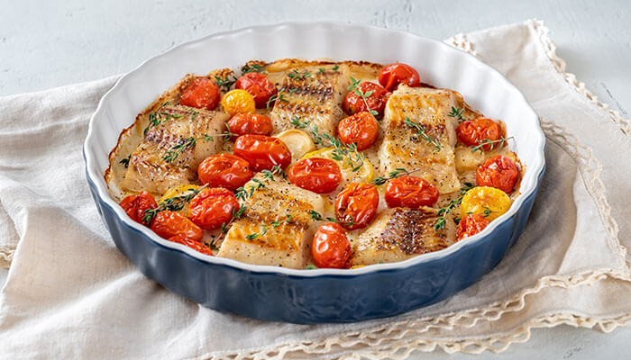 A savory carnivore diet recipe featuring roasted fish fillets with cherry tomatoes and thyme, served in a white baking dish on a soft linen cloth.