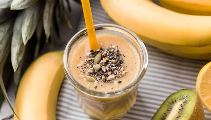 Healthy high protein snacks smoothie topped with chia and pumpkin seeds, surrounded by bananas, kiwi, and fresh fruits.