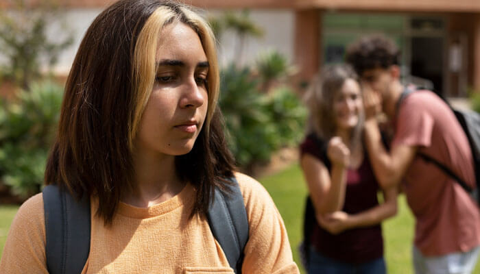 A student feeling left out while others whisper behind her, showing what are some good roasts that may turn hurtful if used without care.