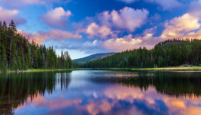 ranquil view of Trillium Lake in Oregon reflecting the surrounding evergreen forest and colorful clouds at sunset, with serene mountain scenery in the background.