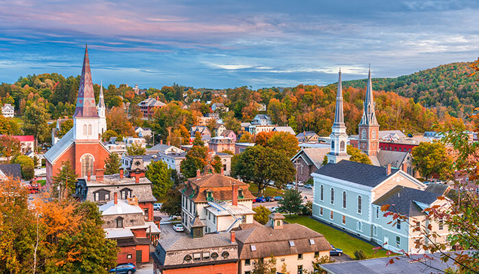 "Charming view of Montpelier, Vermont, featuring historic church steeples, colorful autumn foliage, and classic New England architecture nestled among rolling hills under a soft evening sky.