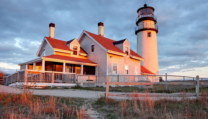 Beautiful view of Highland Light, also known as Cape Cod Lighthouse, in Truro, Massachusetts, illuminated by the warm glow of sunset against a dramatic cloudy sky.