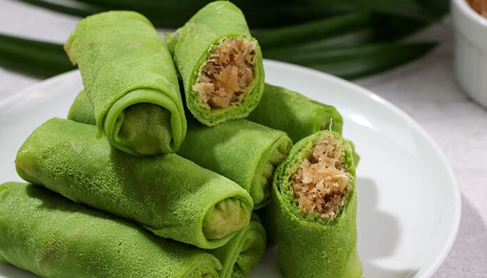 Dadar Gulung Indonesian dessert made of green pandan crepes filled with sweet coconut and palm sugar, neatly stacked on a white plate.