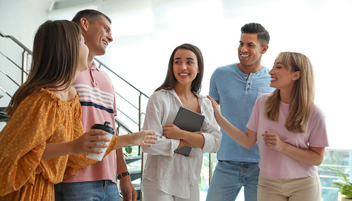 Group of young adults smiling and chatting casually indoors — a friendly moment that shows how asking the right questions to get to know someone can start real connections.