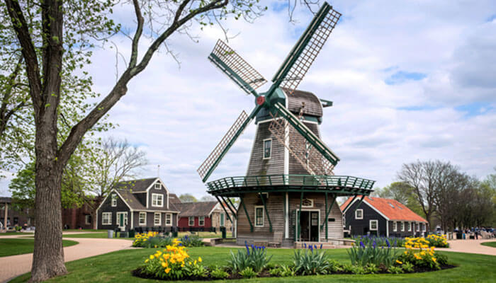 Traditional Dutch-style windmill surrounded by colorful tulips and quaint houses in Holland, Michigan, showcasing the city’s charming Dutch heritage and springtime beauty.