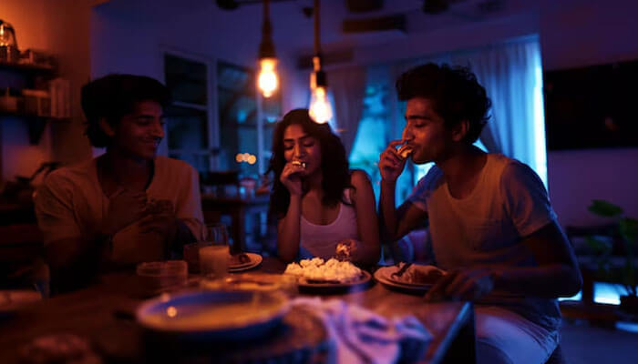 Friends enjoying late night snacks together under warm lighting, sharing food and laughter in a cozy kitchen setting.