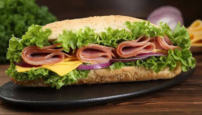 Classic deli sub sandwich with ham, cheddar cheese, red onions, and crisp lettuce on a sesame roll — a fresh and hearty lunch option.