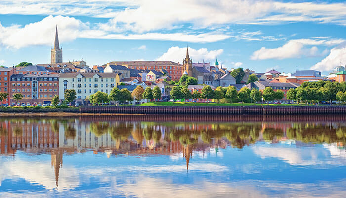 Colorful cityscape of Londonderry with church spires and river reflections, highlighting cultural places to visit in Northern Ireland.