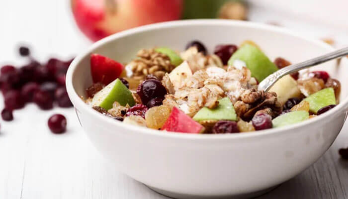 Healthy breakfast bowl with granola, apples, cranberries, and walnuts mixed with yogurt — a wholesome start to the day.