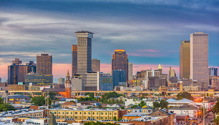 Downtown New Orleans, Louisiana skyline at sunset, featuring modern high-rise buildings, historic architecture, and colorful city rooftops under a vibrant evening sky.