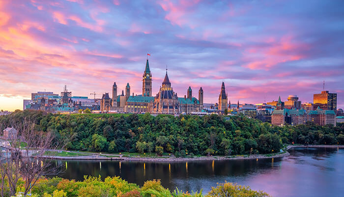 Beautiful view of Ottawa’s Parliament Hill buildings at sunset with pink sky and river — Canada’s capital city landmark.