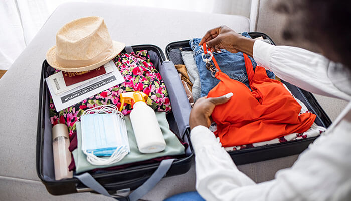 A woman packing summer clothes, skincare, and face masks in a suitcase — an ideal example of what to pack for Europe trip during warm weather.