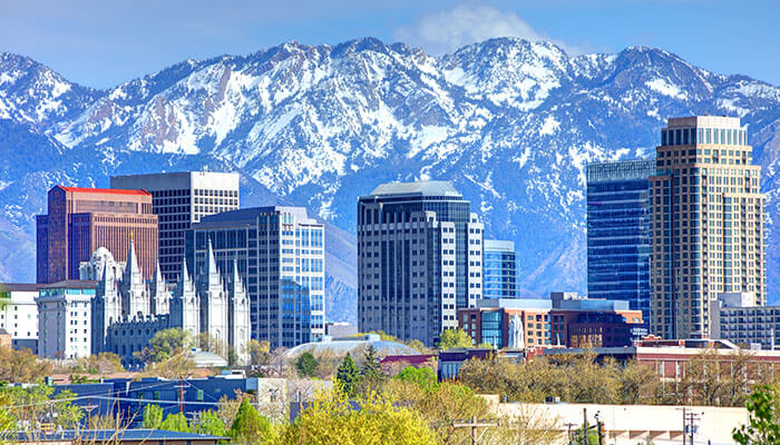 Beautiful view of downtown Salt Lake City, Utah, with modern skyscrapers and the Salt Lake Temple in the foreground, set against the backdrop of the snow-covered Wasatch Mountains.