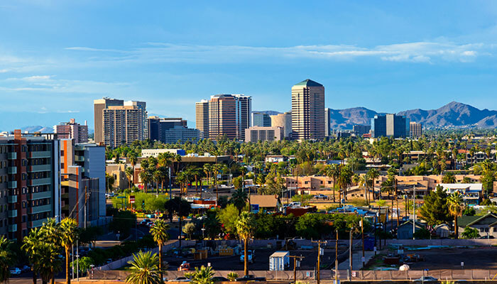 Downtown Scottsdale, Arizona skyline surrounded by palm trees and desert landscape, with the McDowell Mountains in the background under a bright blue sky.