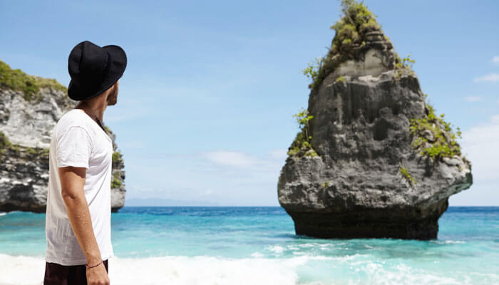 Traveler admiring the iconic rock formations and clear blue sea at Atuh Beach Nusa Penida, a serene and scenic destination in Bali.