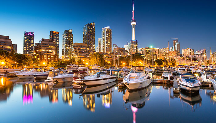 Toronto skyline at night with CN Tower and boats in the harbor reflecting city lights — one of the best places to visit in Canada.