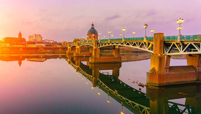 The Pont Neuf bridge in Toulouse glowing at sunset, offering romantic views for travelers on a south of France vacation.