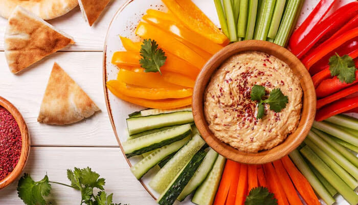 A colorful plate of fresh vegetable sticks with hummus — a healthy and delicious option for late night snacks.
