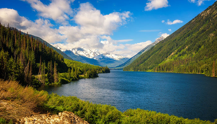 Serene lake surrounded by pine trees and snow-capped mountains in Whistler, British Columbia — a scenic adventure destination.
