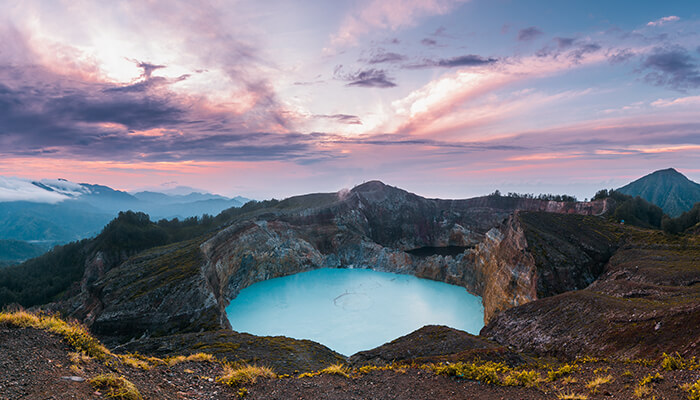 The breathtaking view of Mount Kelimutu’s crater lakes in Flores, Indonesia, with vibrant turquoise water and a colorful sunrise sky.