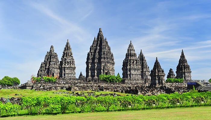 The majestic Prambanan Temple complex in Java, Indonesia, with towering spires set against a bright blue sky and green surroundings.