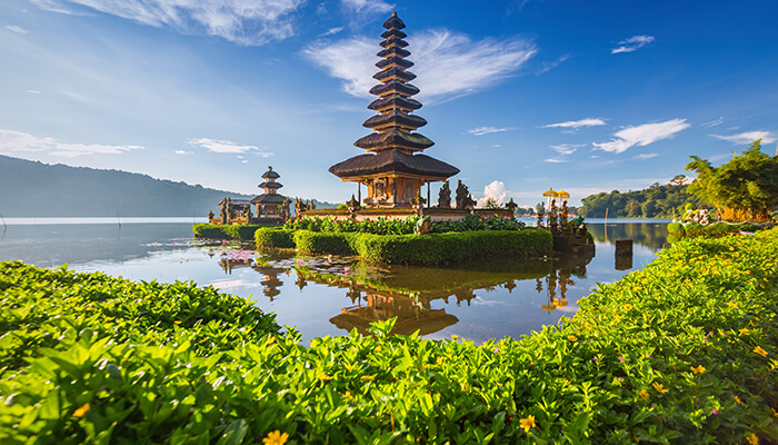 A serene view of the Ulun Danu Beratan Temple in Bali, with its pagoda-style architecture reflecting in the tranquil waters surrounded by lush green foliage.
