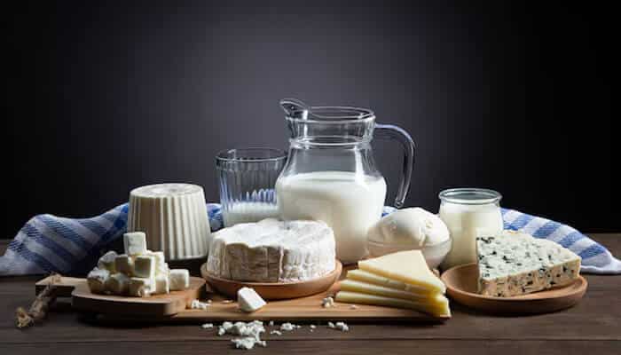 A variety of dairy products including milk, cheese, yogurt, and soft cheeses arranged on a wooden board.