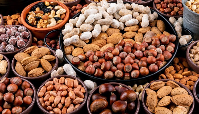 An assortment of nuts such as almonds, hazelnuts, peanuts, and coated nuts displayed in bowls and trays