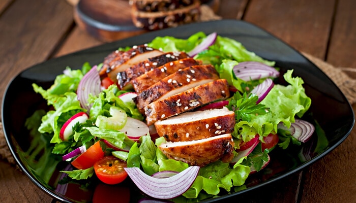 The healthy chicken salad recipes to know - Food Fun Trip - FoodFunTrip Grilled chicken slices served on a fresh salad with mixed greens, tomatoes, and onions, providing a healthy and satisfying meal