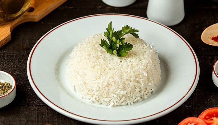 A plate of steamed white rice garnished with parsley, shown as one of the simple high calorie foods for meal preparation.