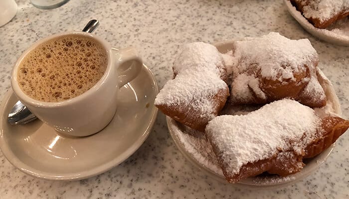 Enjoy Beignets at Cafe du Monde - Food Fun Trip - FoodFunTrip A plate of beignets dusted with powdered sugar and a cup of coffee, iconic treats from Café du Monde in New Orleans