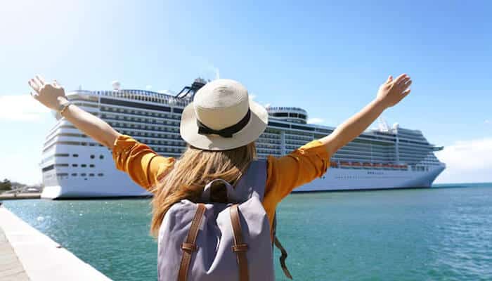 Vacations to Go Cruises Your Guide to an Unforgettable Journey - Food Fun Trip - FoodFunTrip Traveler raising her arms in front of a luxury cruise ship booked through Vacations to Go