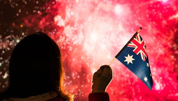 Curated Travel Options for Festival Experiences - Food Fun Trip - FoodFunTrip Person seen from behind waving an Australian flag with bright red fireworks in the background.