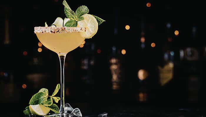 Garnishing and Presentation - Food Fun Trip - FoodFunTrip A margarita-style cocktail in a salted-rim coupe glass with a lime wedge and mint garnish on a dark bar backdrop.