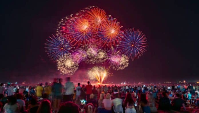 Crowd of people watching a colorful fireworks display lighting up the night sky over a beach.