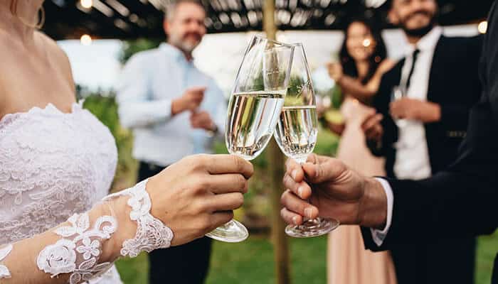 Add One Small Detail Guests Will Remember - Food Fun Trip - FoodFunTrip Bride in a lace wedding gown toasts with champagne flutes, clinking with guests at an outdoor wedding reception.