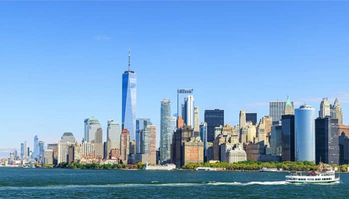 New York City skyline across a blue harbor with One World Trade Center and a ferry in the foreground