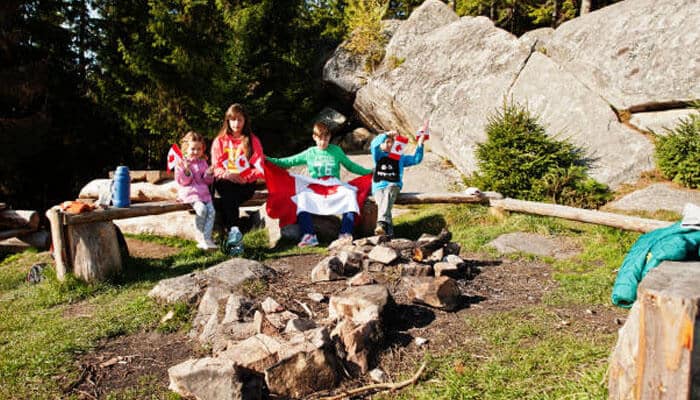 Planning Your Family Stay at Montreal South KOA Journey - Food Fun Trip - FoodFunTrip Family enjoying a Montreal camping experience near a campfire with Canadian flags, rocky nature scenery, and kid-friendly outdoor fun.