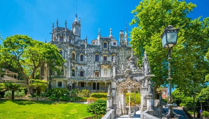 Practical Tips for Your Visit - Food Fun Trip - FoodFunTrip Quinta da Regaleira in Sintra, Portugal, featuring Gothic revival architecture, ornate towers, lush gardens, and symbolic statues under a clear blue sky.