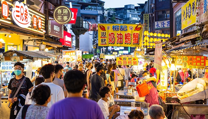 Taiwans Essential Food Institution - Food Fun Trip - FoodFunTrip Taiwan Food night market scene with busy street stalls, glowing signs, local snacks, and travelers exploring authentic Taiwanese street cuisine.