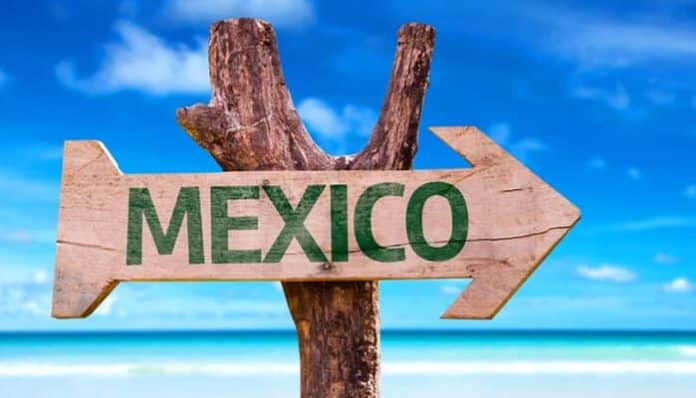 Wooden sign pointing to Mexico on a sunny beach with turquoise waters, symbolizing travel, tourism, and tropical vacation destinations in Mexico
