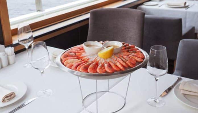 Shrimp platter arranged in a circle around a lemon wedge on a metal stand at a fine-dining table with glassware nearby